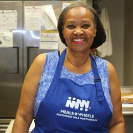 Woman in a kitchen wearing an apron that says Meals on Wheels of Southwest OH and Northern KY